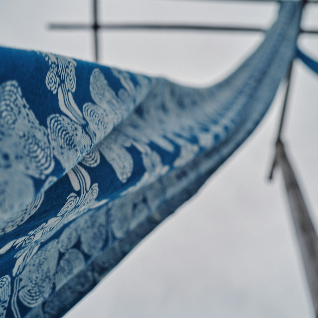 A blue and white patterned fabric hanging on a wooden frame outdoors.