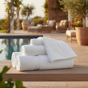 Stack of white towels on a wooden table by a poolside with a floral arch in the background.