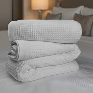 Stack of white textured blankets on a bed with a blurred bedroom background