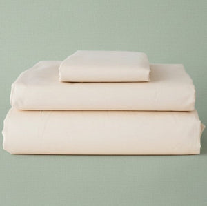 Stack of beige folded bed sheets on a light green background | By Rifz Textiles 