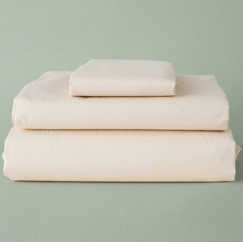 Stack of beige folded bed sheets on a light green background | By Rifz Textiles 