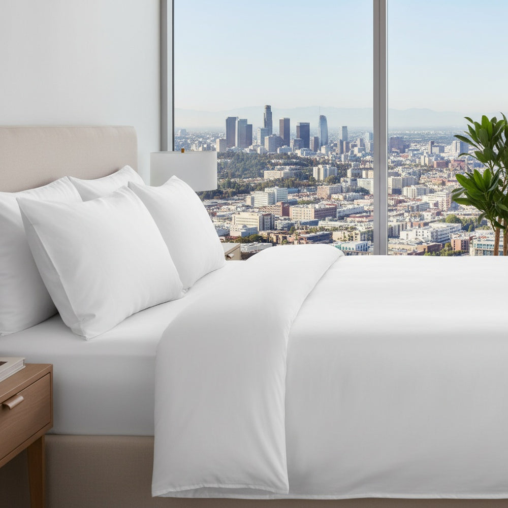 Bedroom with white bedding and a cityscape view through large windows.