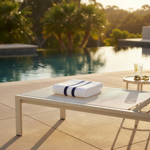 Folded towel on a lounge chair by a pool with trees in the background